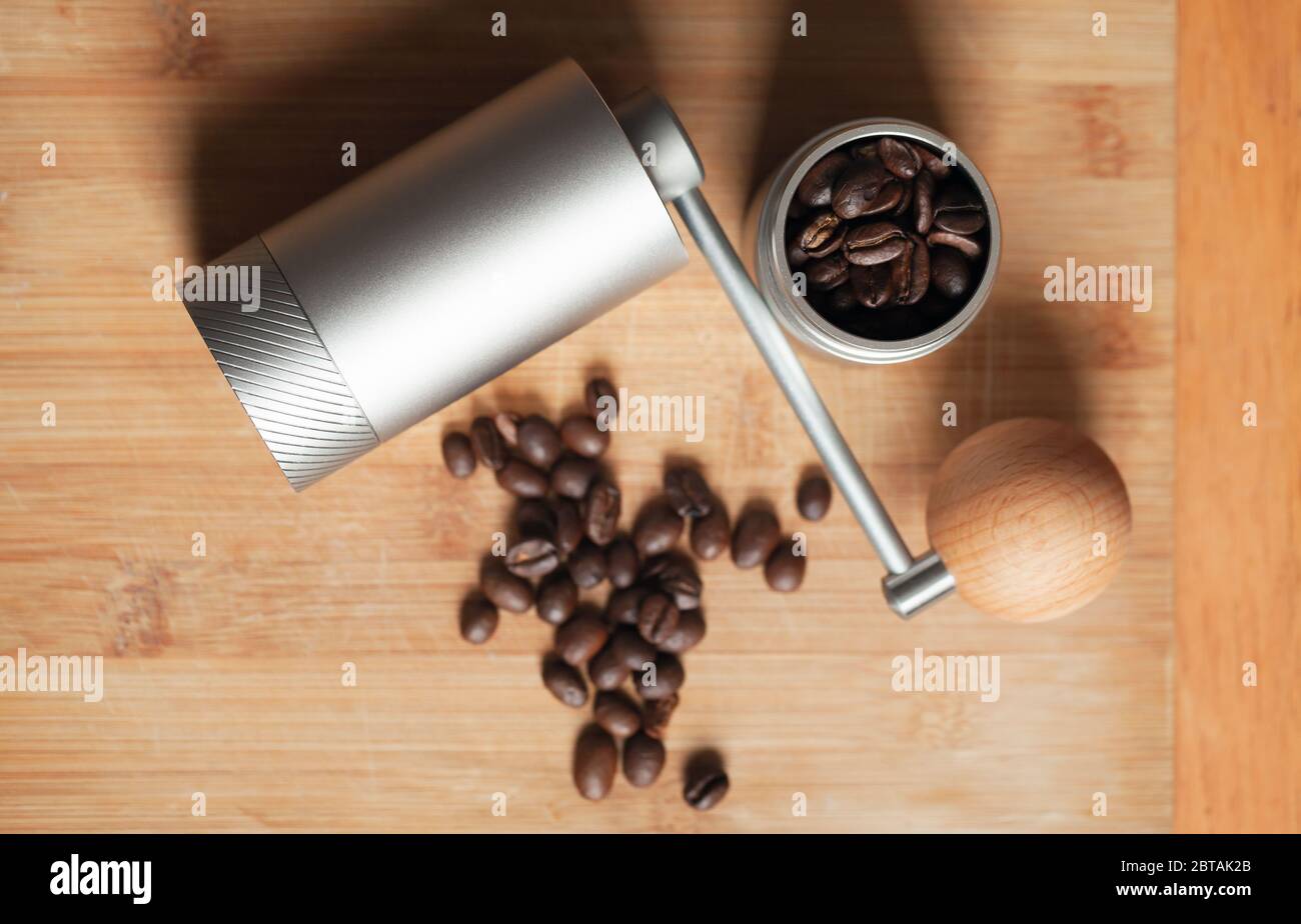 Shiny manual coffee grinder and roasted coffee beans are on wooden desk, close-up top view photo with selective focus Stock Photo