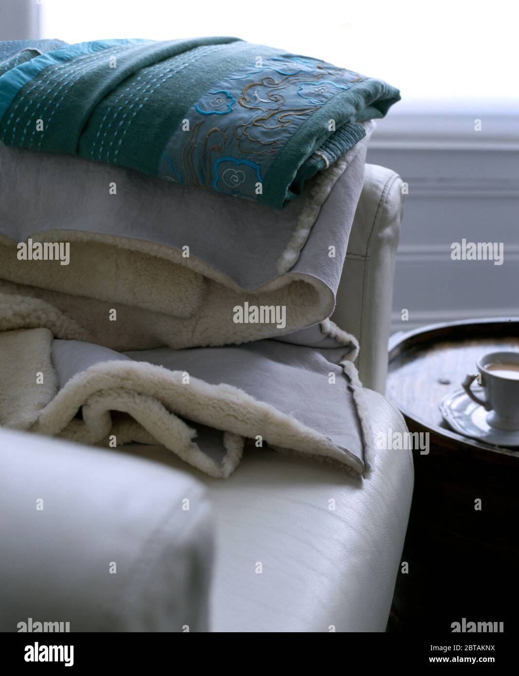 Blue cotton and sheepskin throws on white leather armchair Stock Photo