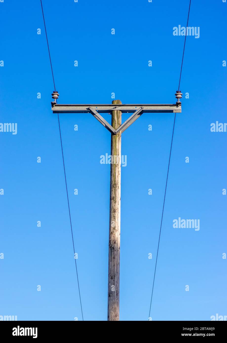 Two power lines on insulators on a wooden telegraph pole with a blue background Stock Photo