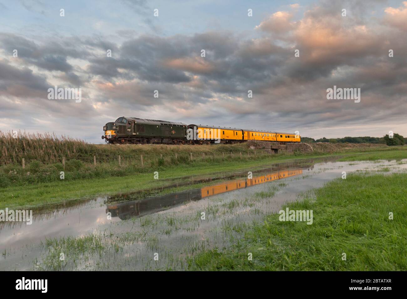 Colas class 37 locomotive 37057 in British Rail Green hauling a Network Rail infrastructure monitoring train reflected in a flooded field Stock Photo