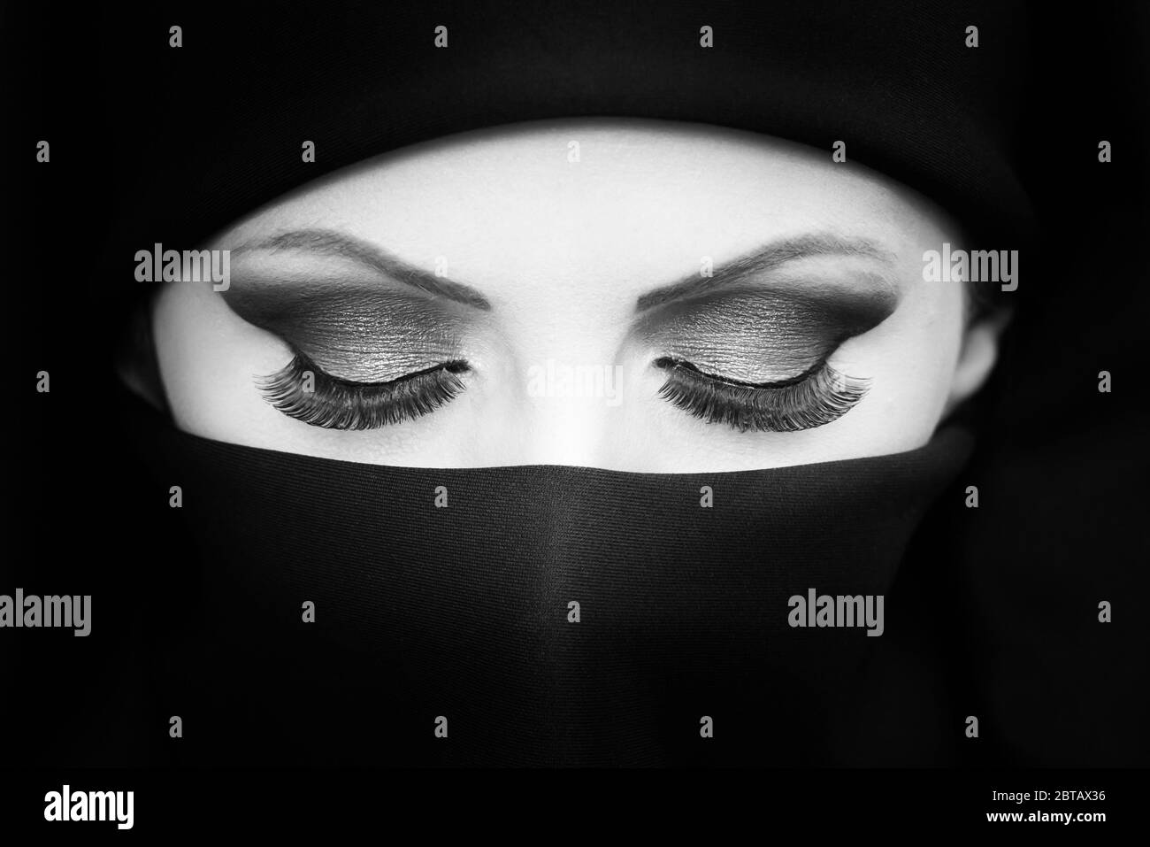 Black and white portrait of beautiful young Asian girl/woman with niqab highlighting makeup and long eyelashes. Stock Photo