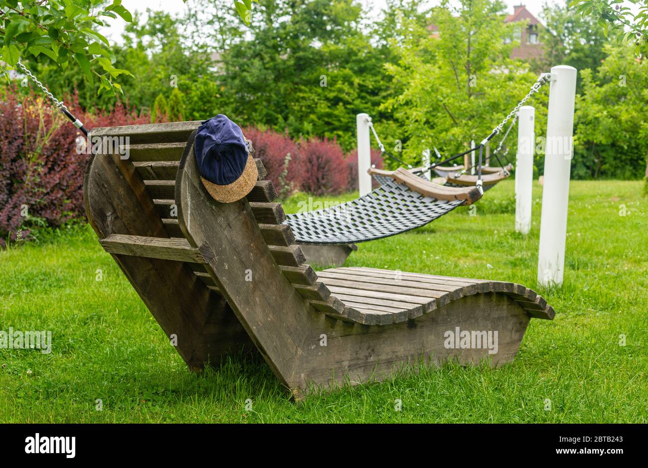 Hat on the bench. Loungers in the park. Wooden furniture. Recreational areas in the city. Time to relax. Family walks. Municipal greenery. Stock Photo