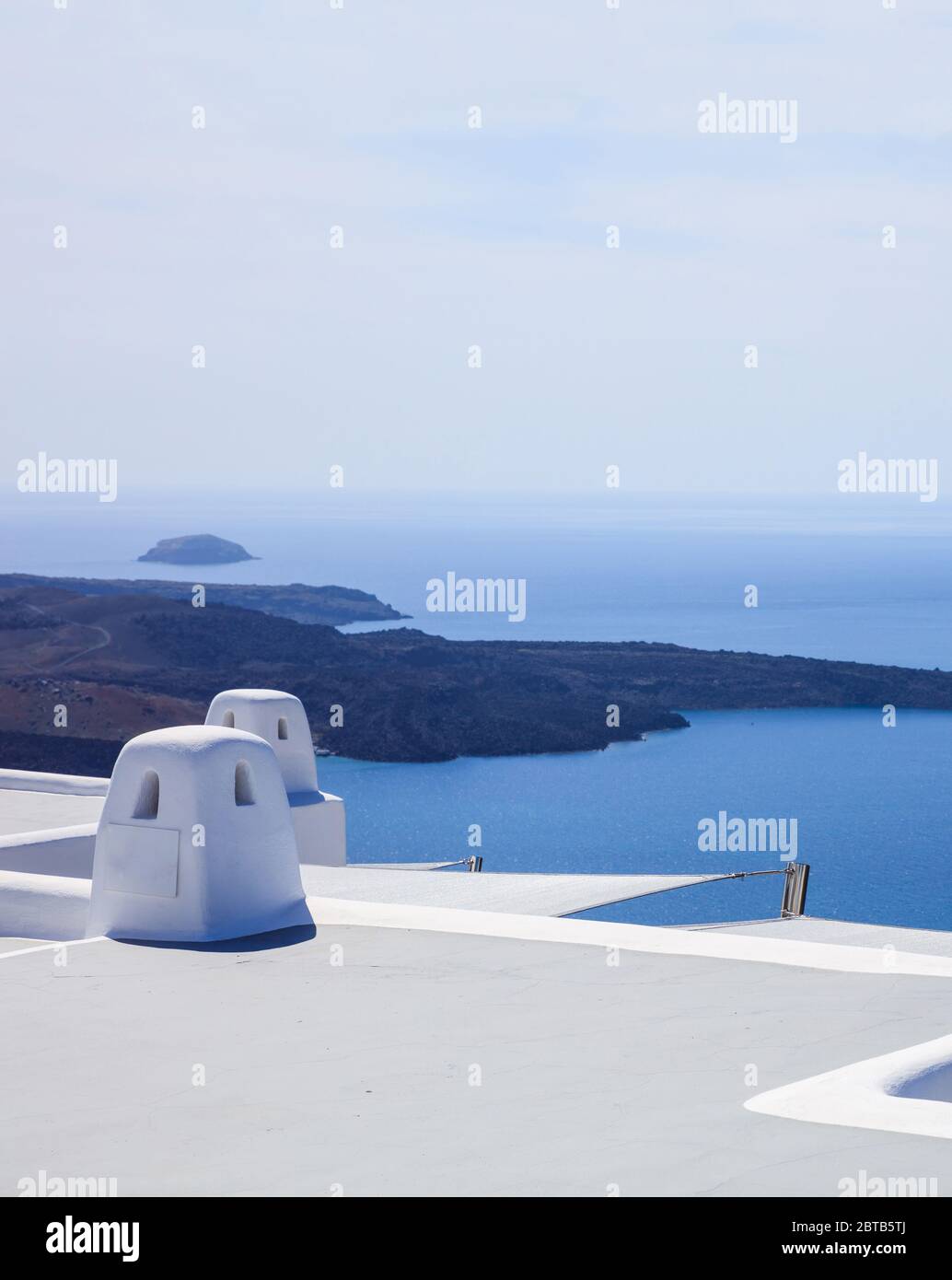 Santorini island, Greece, White terrace and traditional chimney on caldera overlooking the sea. White architecture against blue sea and clear sky back Stock Photo