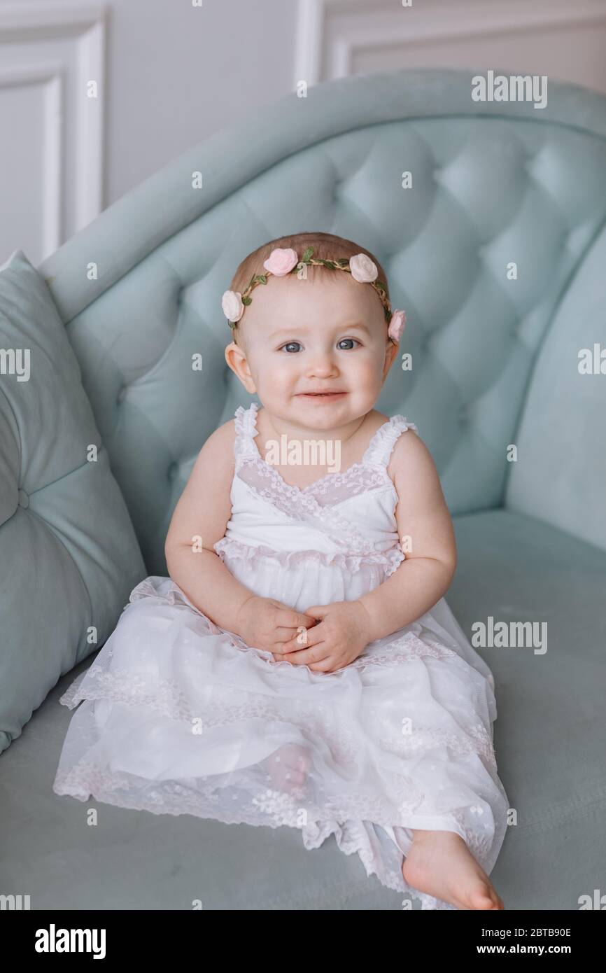 cute little girl in white dress and hoops of flowers on head is sitting ...
