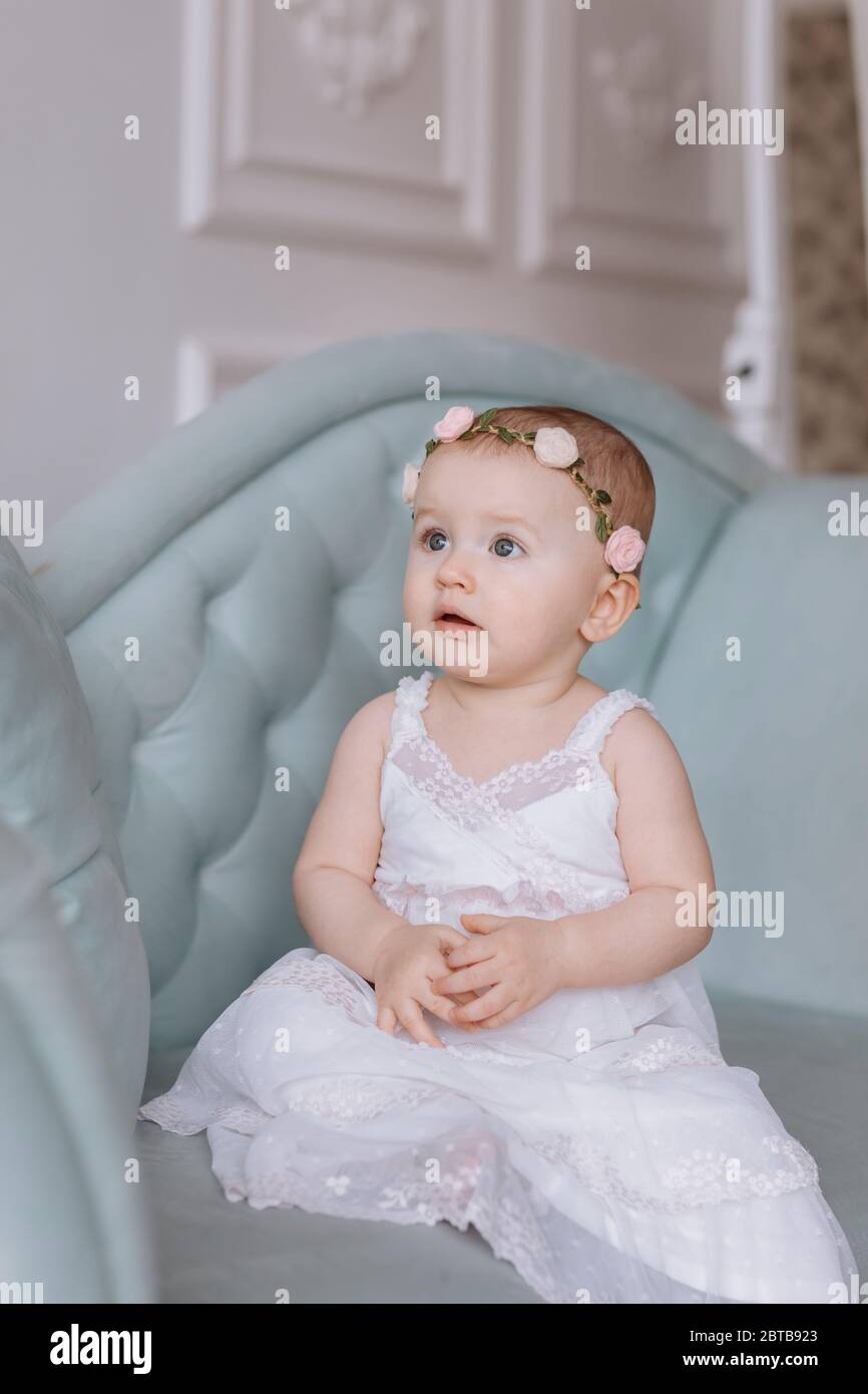 cute little girl in white dress and hoops of flowers on head is sitting ...