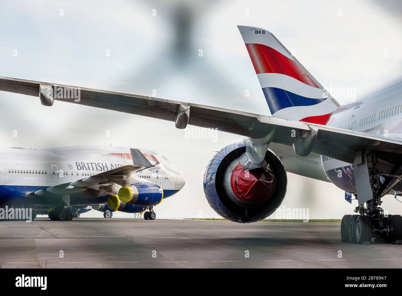 Seen through a wire fence, British Airways aeroplanes are parked at Cardiff Airport whilst unused during the Covid-19 crises. Stock Photo
