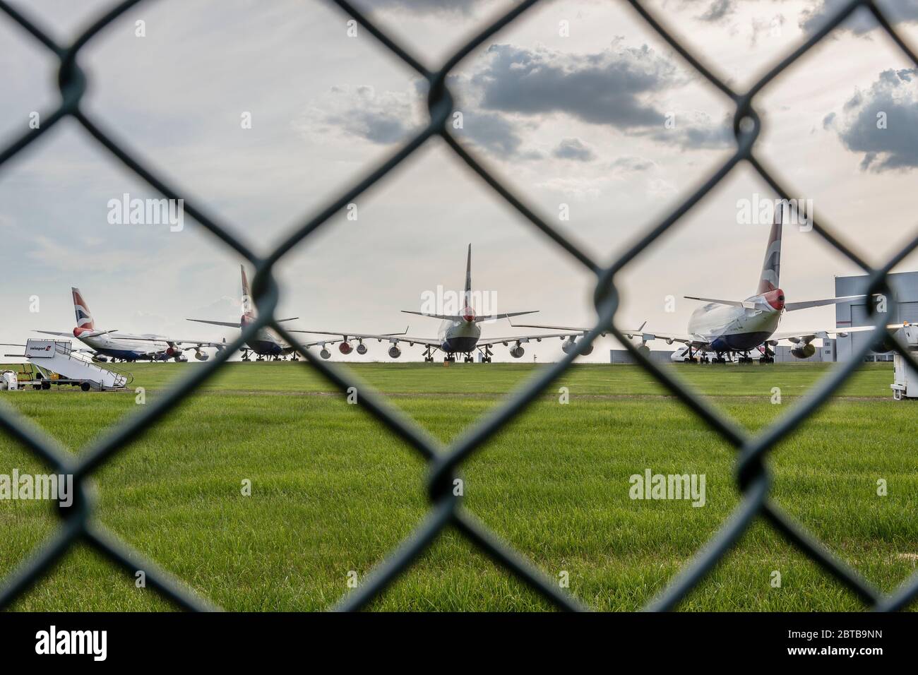 Seen through a wire fence, British Airways aeroplanes are parked at Cardiff Airport whilst unused during the Covid-19 crises. Stock Photo