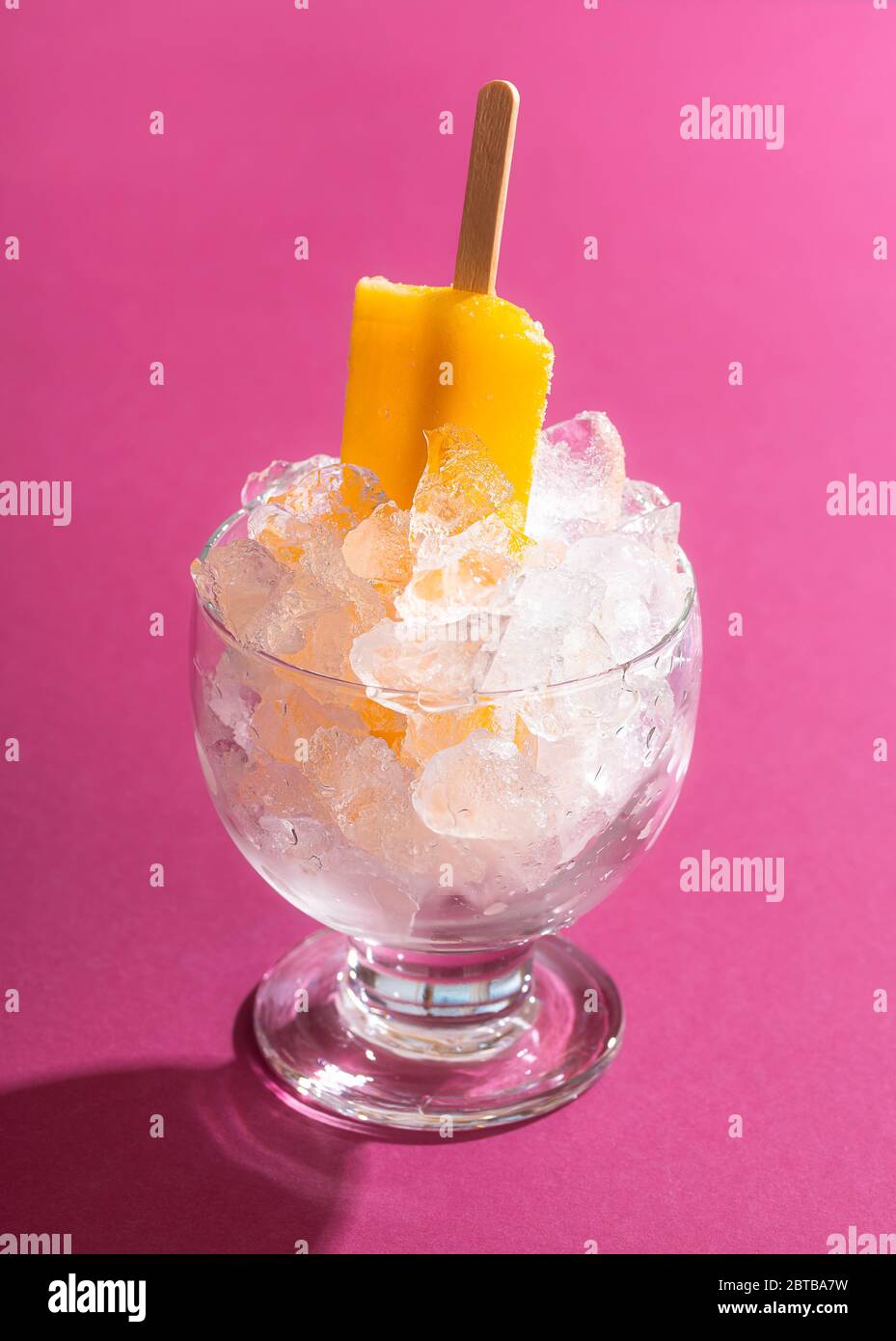 Orange ice cream popsicle in a bowl with crushed ice on a pink seamless background in harsh light. Cooling summer dessert. Vegan ice cream on stick. Stock Photo