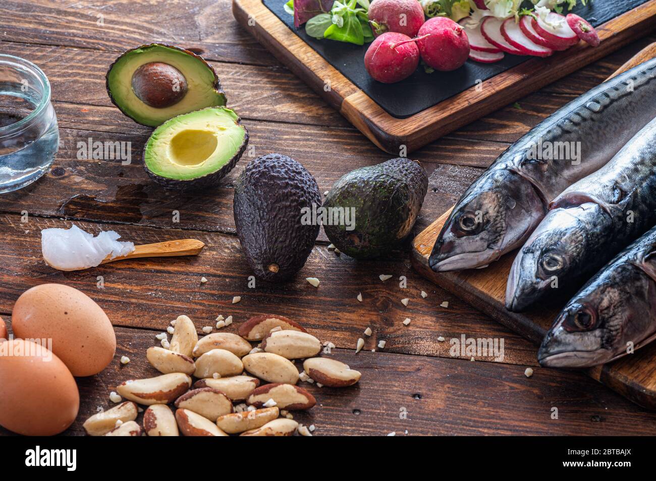 Close up of ketogenic food: MCT oil, mackerel fish, avocado, eggs, coconut butter, Brazilian nuts, radishes, Omega-3 supplements on a wooden table Stock Photo
