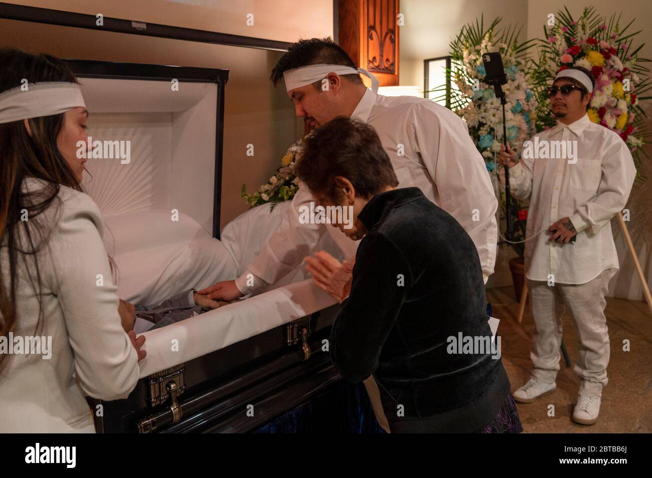 Sacramento, California, USA. 6th May, 2020. Bao Nguyen films the funeral of  his father Dung Tan Nguyen as his brother Michael Chambon gives one last  touch alongside Trang Nguyen, left, and Kim