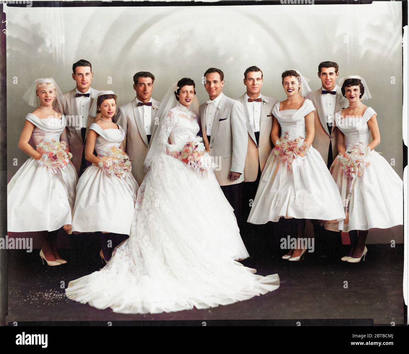 1958 ca, CHICAGO , USA  : A wedding dress of italian immigrants of 2nd generation born in USA . Photo by Universal Studio , Chicago . COLORIZED DIGITALLY . - NOZZE - abito da SPOSA - WEDDING dress PARTY - BRIDE -  cerimonia   - FOTO STORICHE - HISTORY PHOTOS - XX CENTURY - NOVECENTO  - thulle - tulle - strascico  - FAMIGLIA - FAMILY - PARENTI - festa - party - ricevimento  - velo - veil - flowers - fiori - fiore - carnations - garofano - garofani  - IMMIGRATI ITALIANI - ITALO-AMERICANI - seconda generazione - smile - sorriso - papillon - tie bow - cravatta - white dress - abito vestito bianco Stock Photo