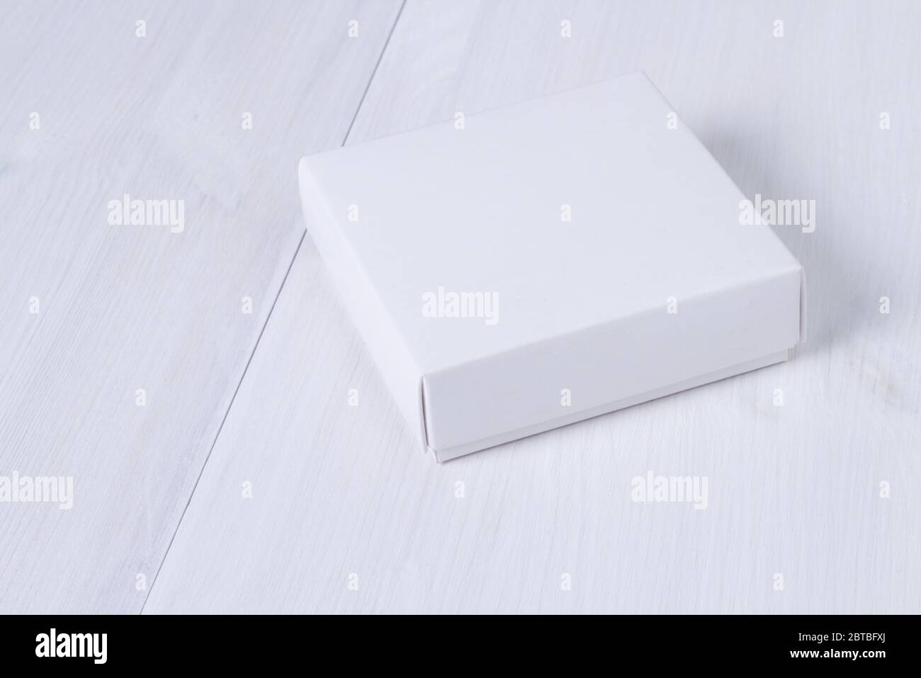 White box on wooden white table. Stock photo. White box mockup for product and advertising with cover on white wooden background. Side view. Delivery Stock Photo