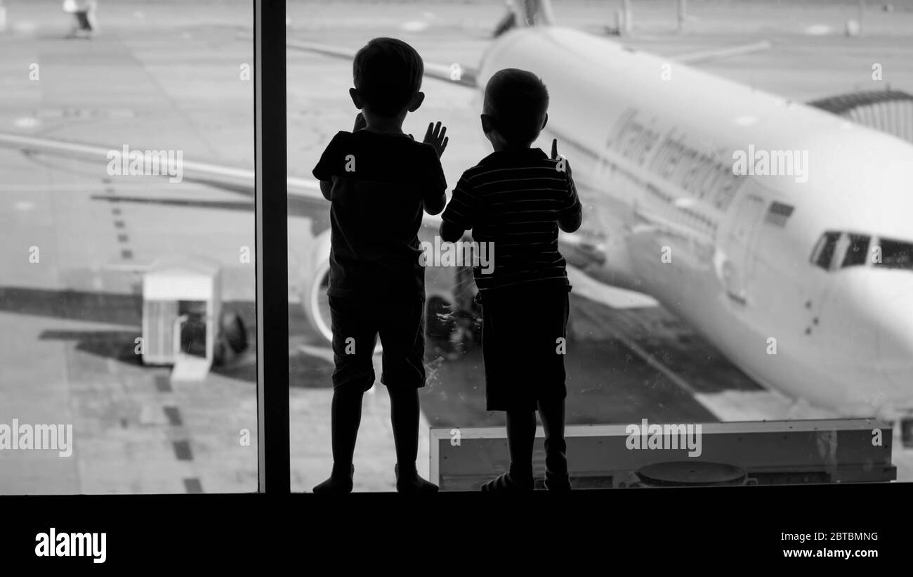 Black and white image of boys silhouettes looking on big airplane parked in airport terminal Stock Photo