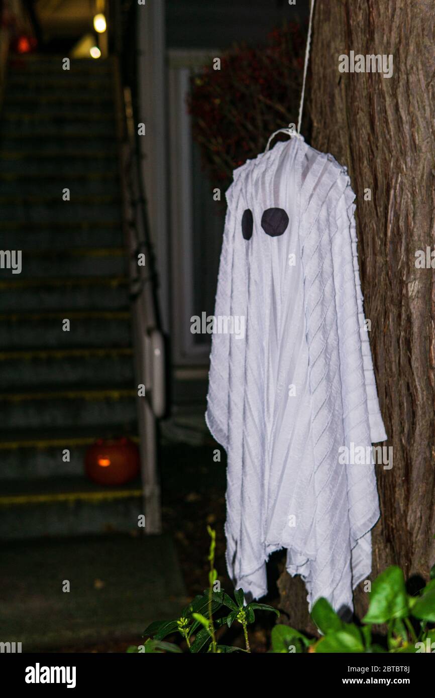 white ghost hanging on a tree during a holiday for Halloween on dark background. Stock Photo