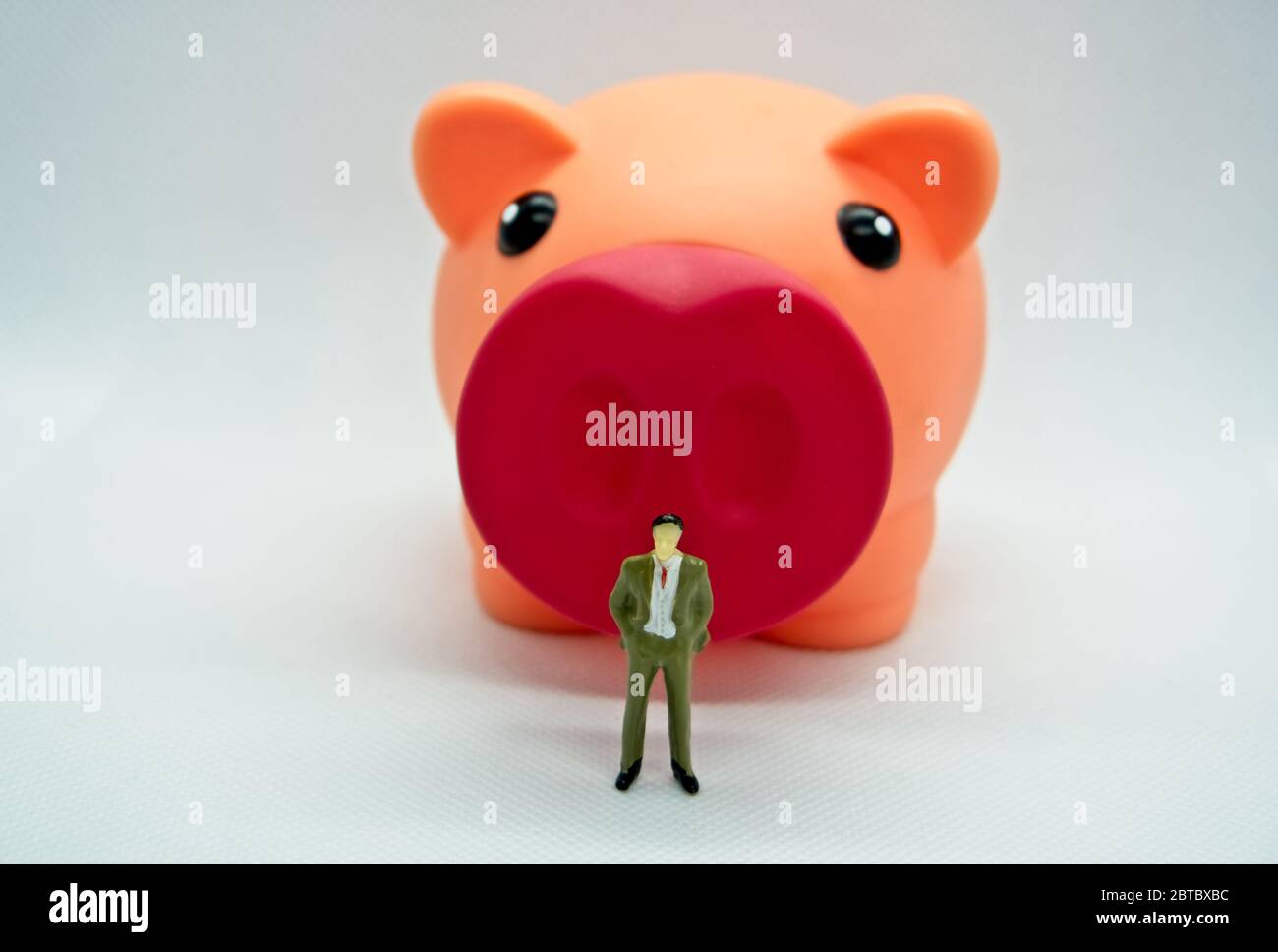 Figure of a man standing in front of a piggy bank in a white background ...