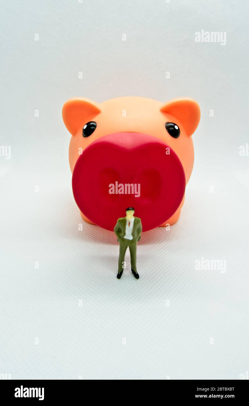 Figure of a man standing in front of a piggy bank in a white background ...