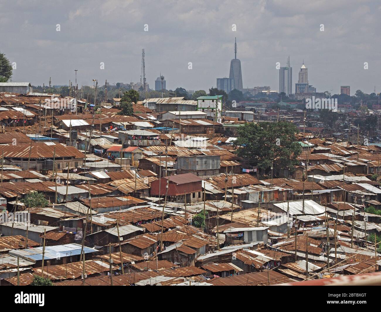 view over the tin roofs of the infamous Kibera slum district towards a skyline of modern skyscraper buildings of 21st century Nairobi in Kenya, Africa Stock Photo