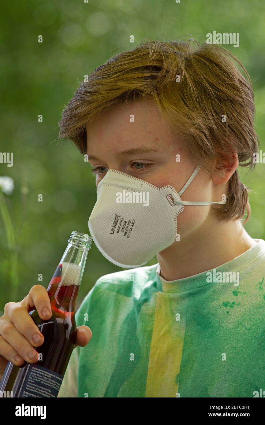 boy wearing breathing mask trying to drink from a bottle, Germany Stock Photo