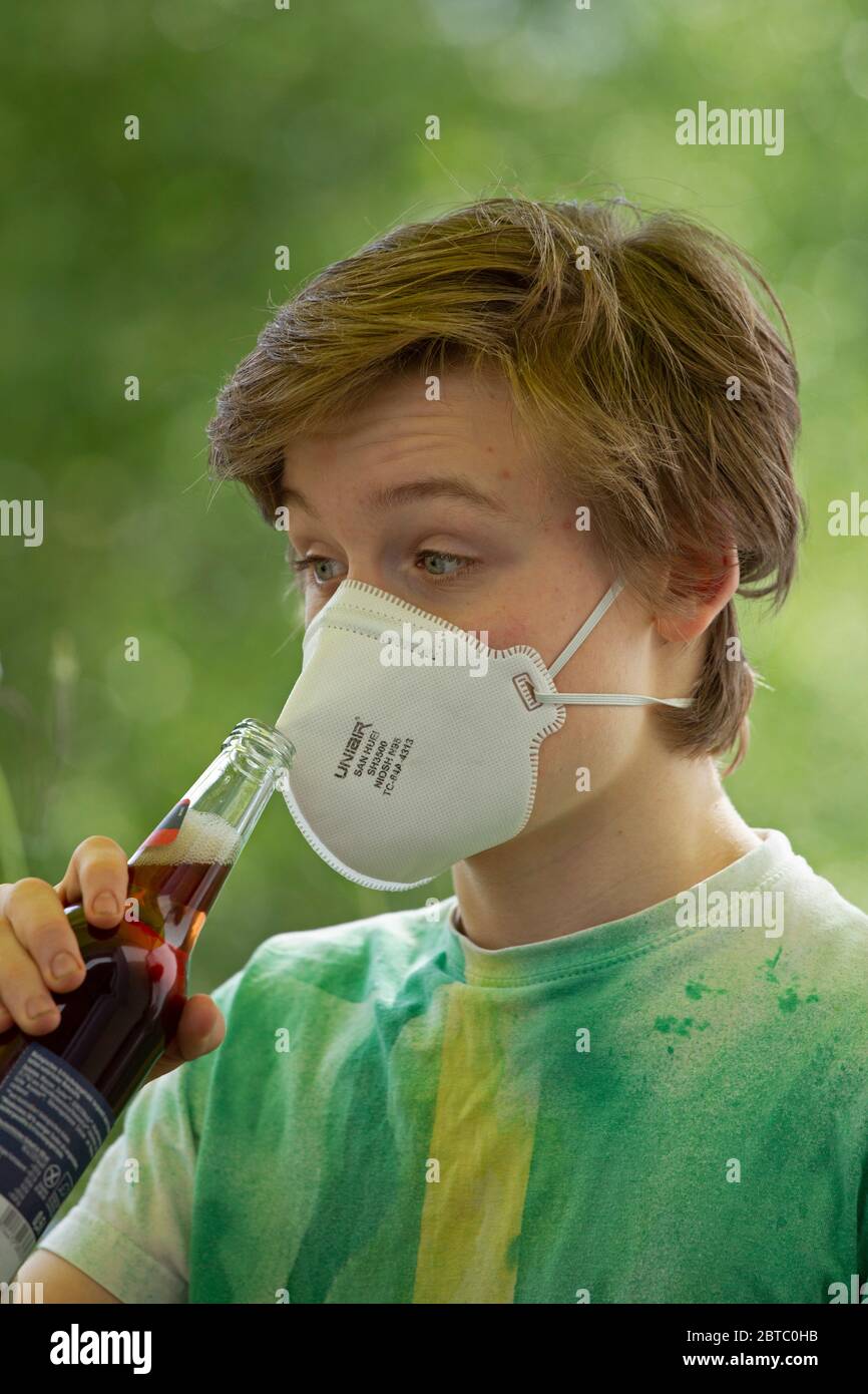 boy wearing breathing mask trying to drink from a bottle, Germany Stock Photo