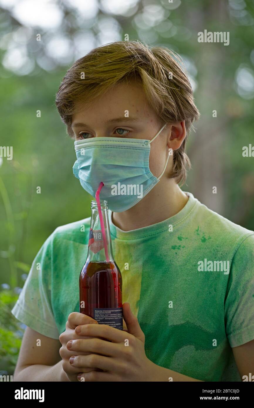 boy wearing breathing mask drinking from a bottle using a straw, Germany Stock Photo