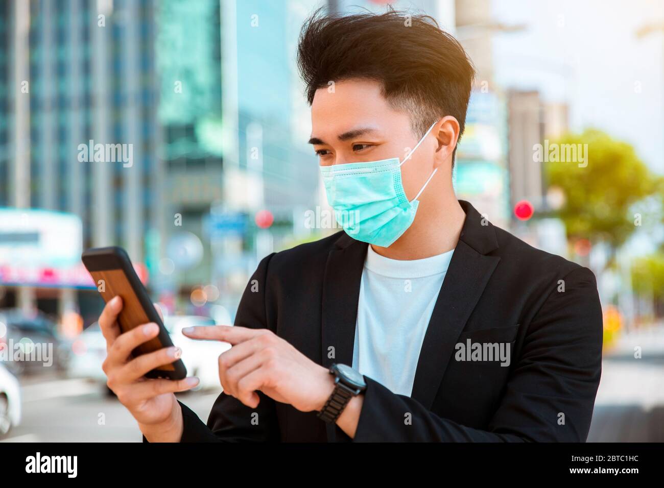 young business man wearing a mask on the street and twatching the ...
