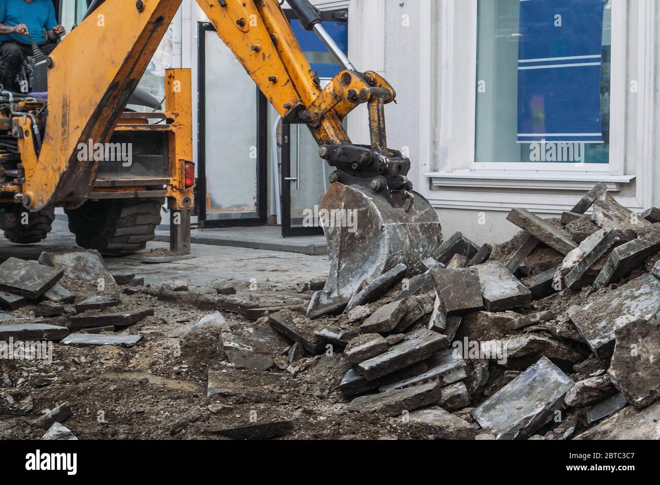 Excavator bucket breaks paving slabs. Sidewalk dismantling and repair work in city. Stock Photo