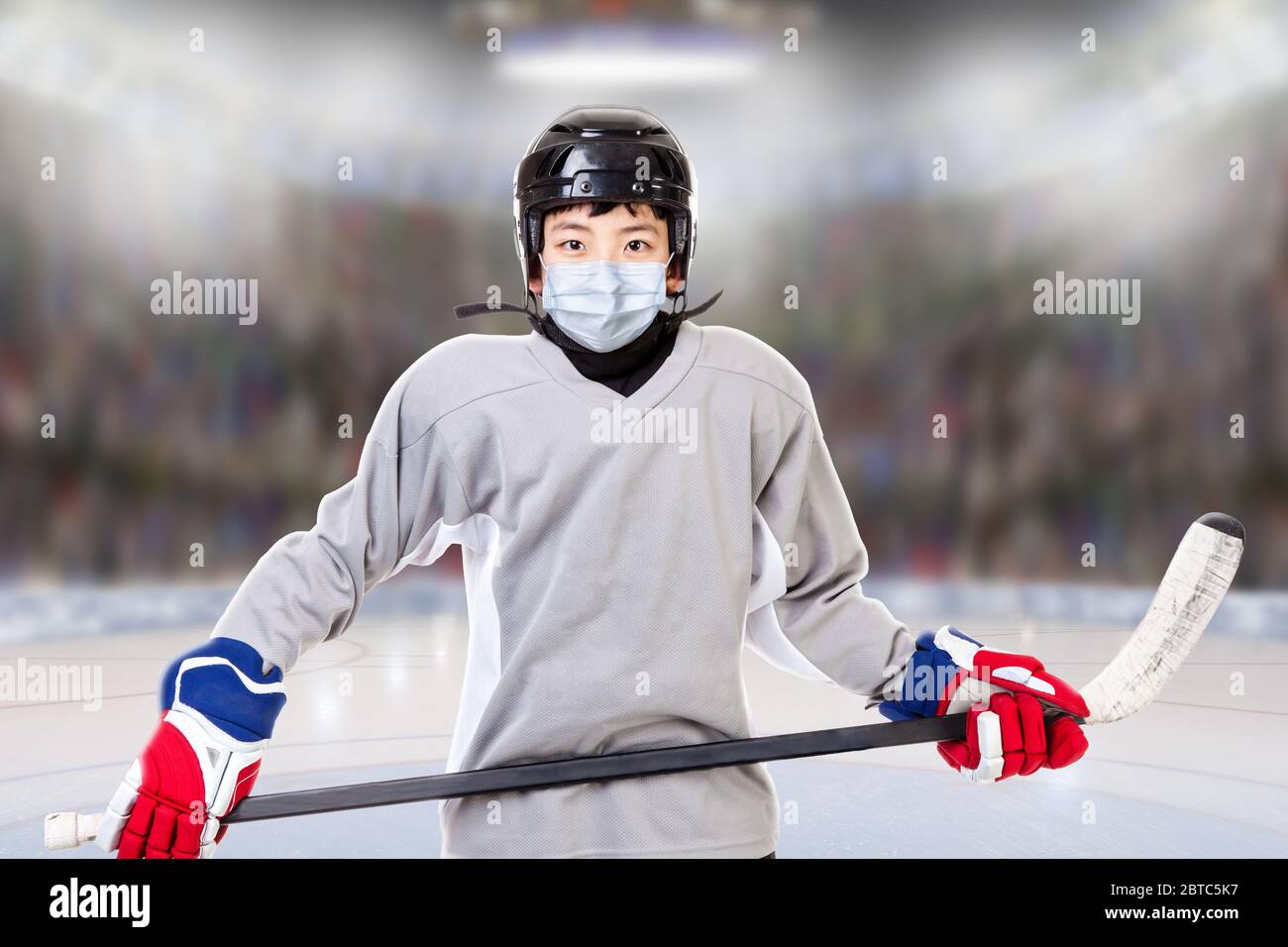 Junior ice hockey player with full equipment and sports uniform posing in fictitious arena with face mask. Concept of new normal in sports to prevent Stock Photo