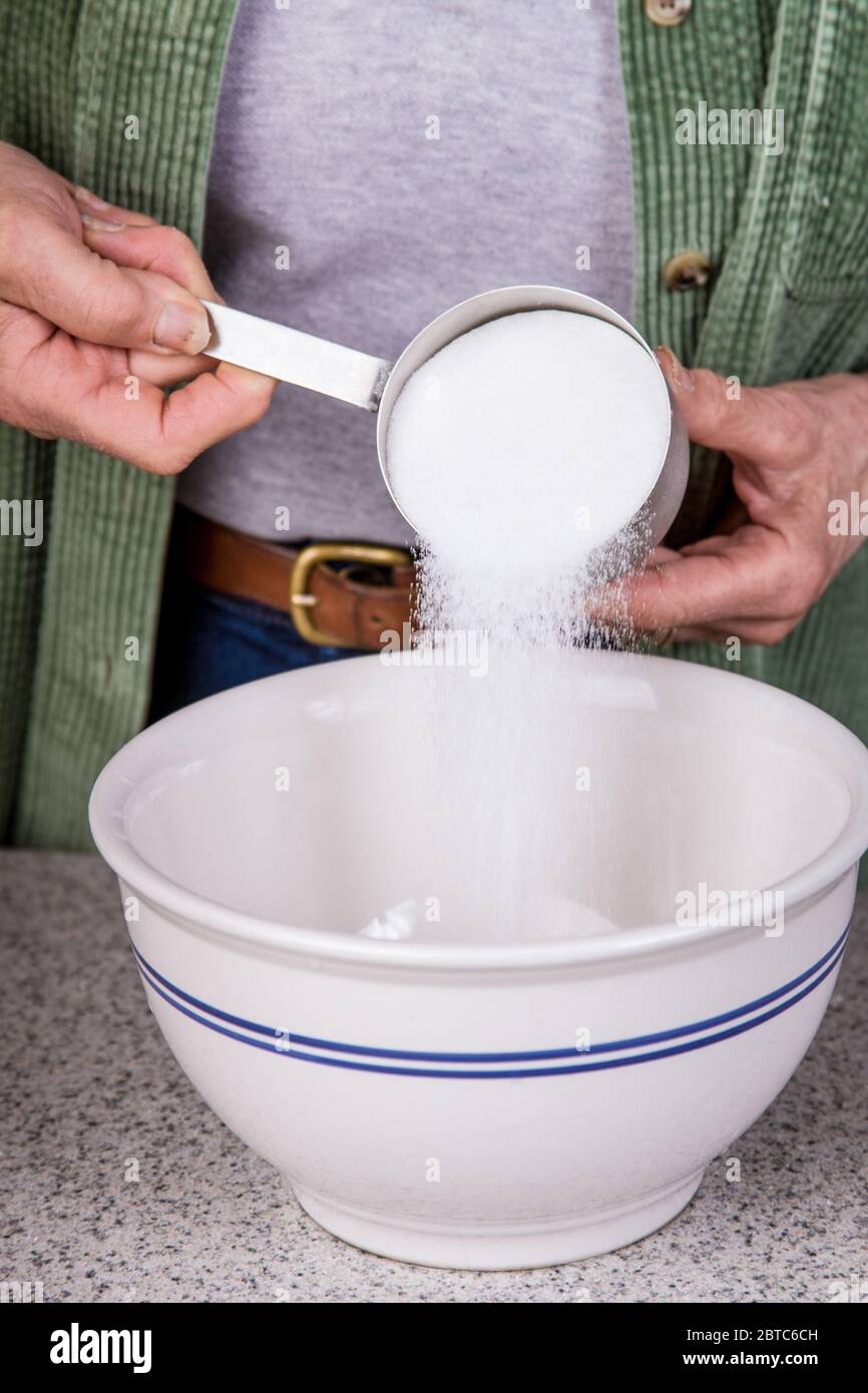 Woman pouring sugar into a mixing bowl as part of making monkey bread Stock Photo