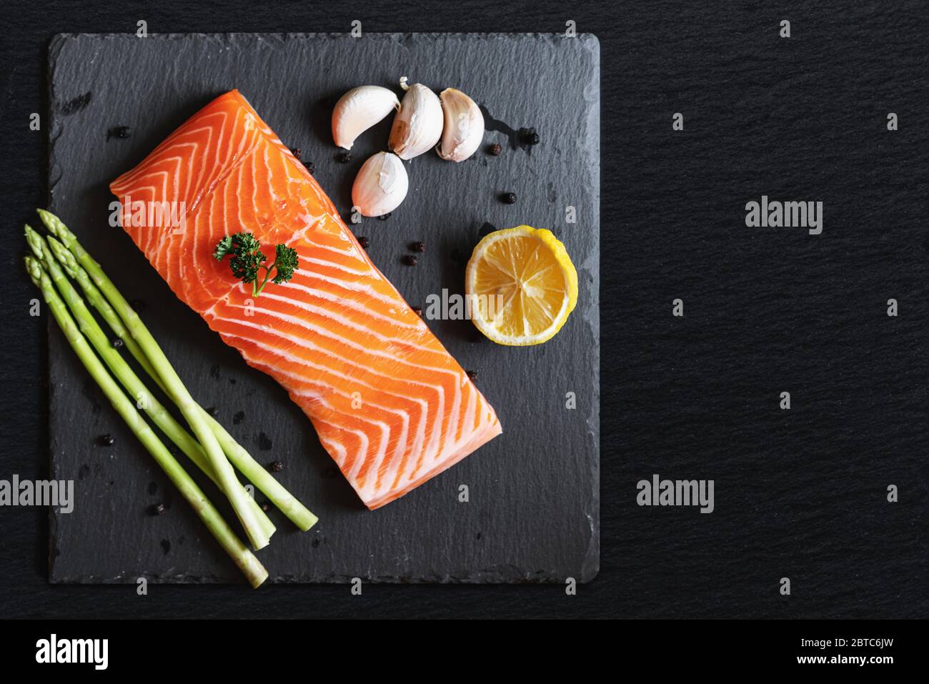 Raw fresh salmon fillet with herbs and ingredients, on black stone plate with copy space Stock Photo