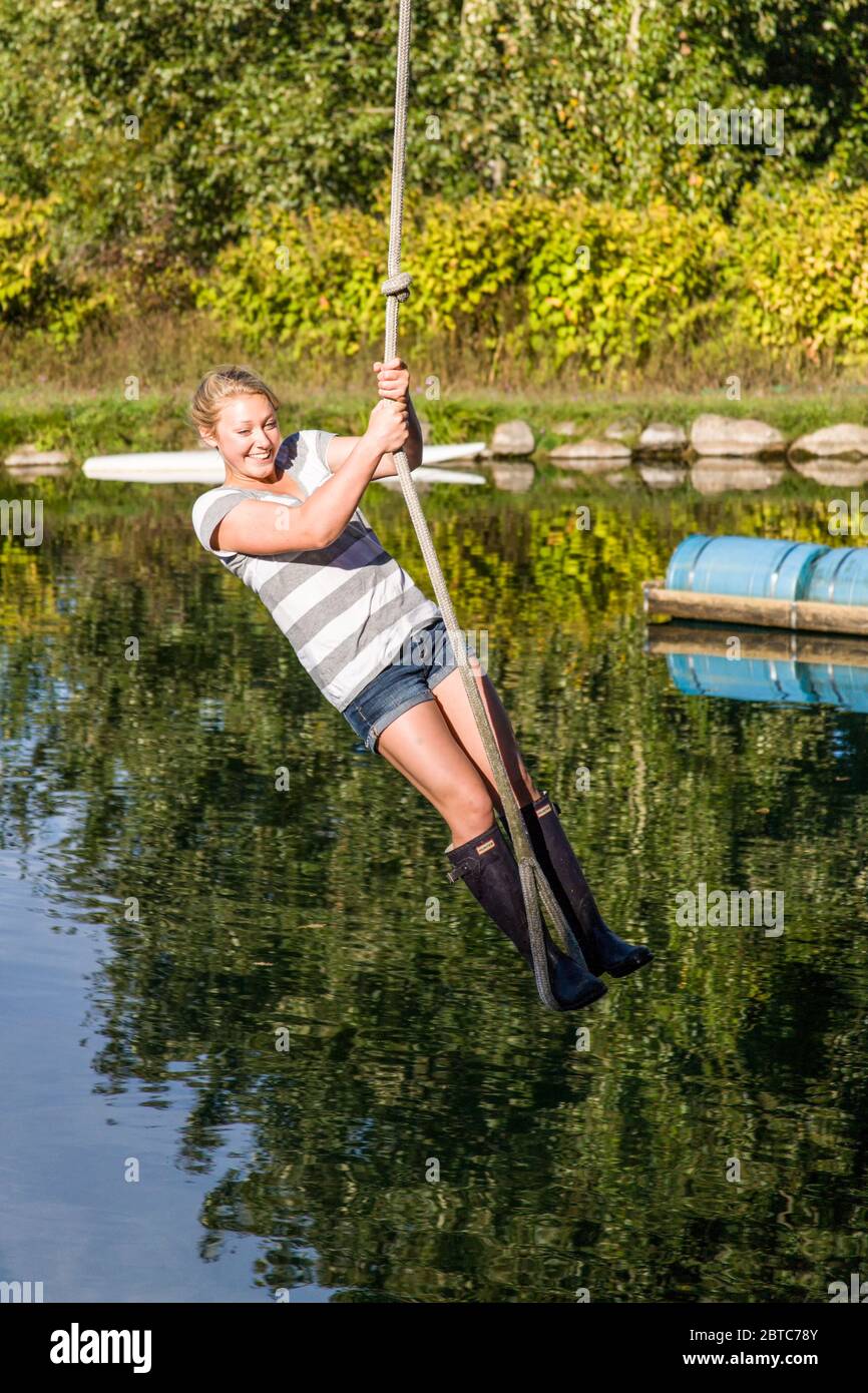 Young woman enjoying swinging on a rope swing over a farm pond at