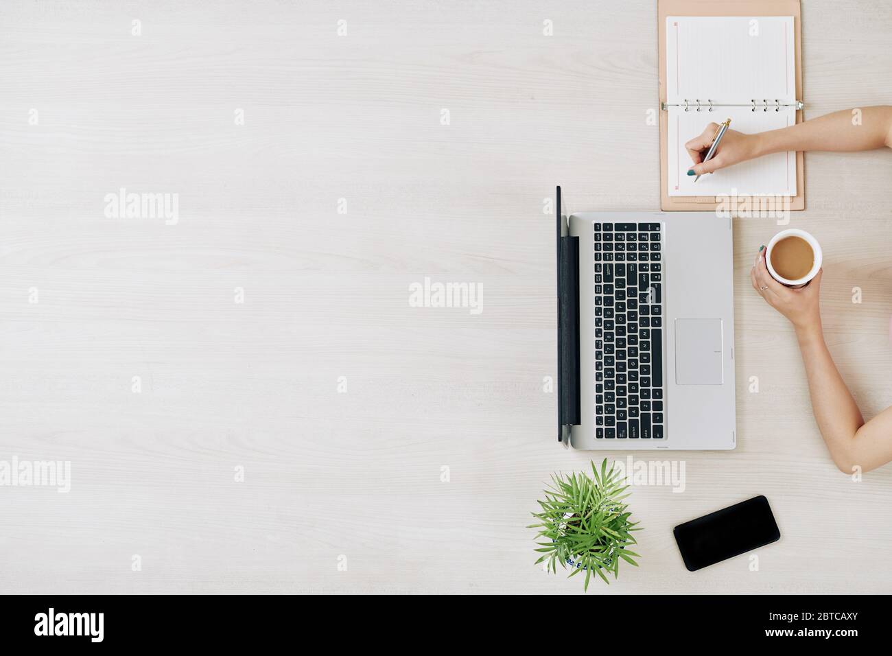 Female freelancer working at big office table, drinking coffee and taking notes in planner Stock Photo