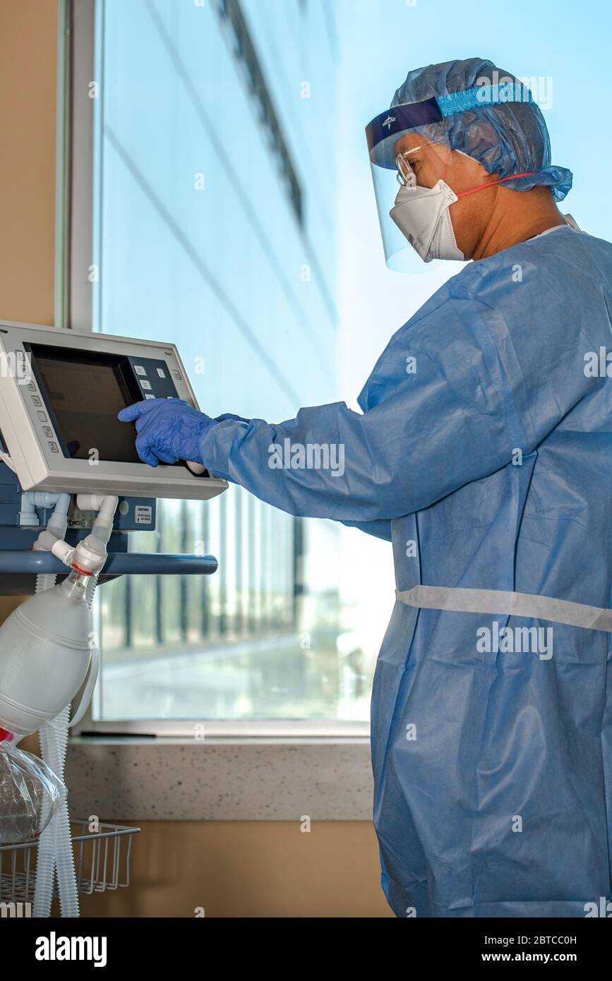 A Respiratory Therapist dressed in full protective gear in an intensive care adjusts ventilator settings during the corona virus pandemic. Stock Photo
