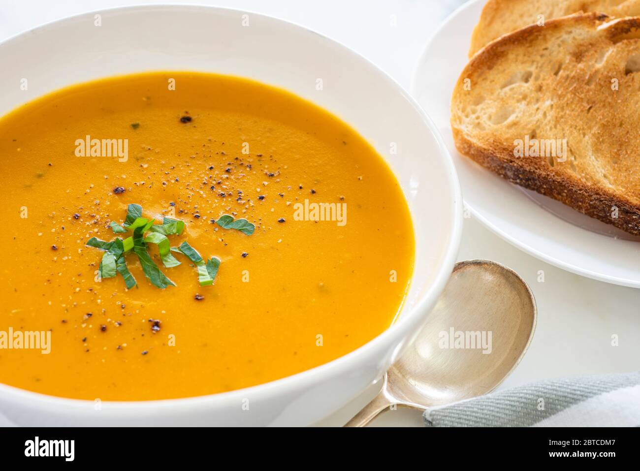Pumpkin soup in white bowl with toasted bread on the side Stock Photo