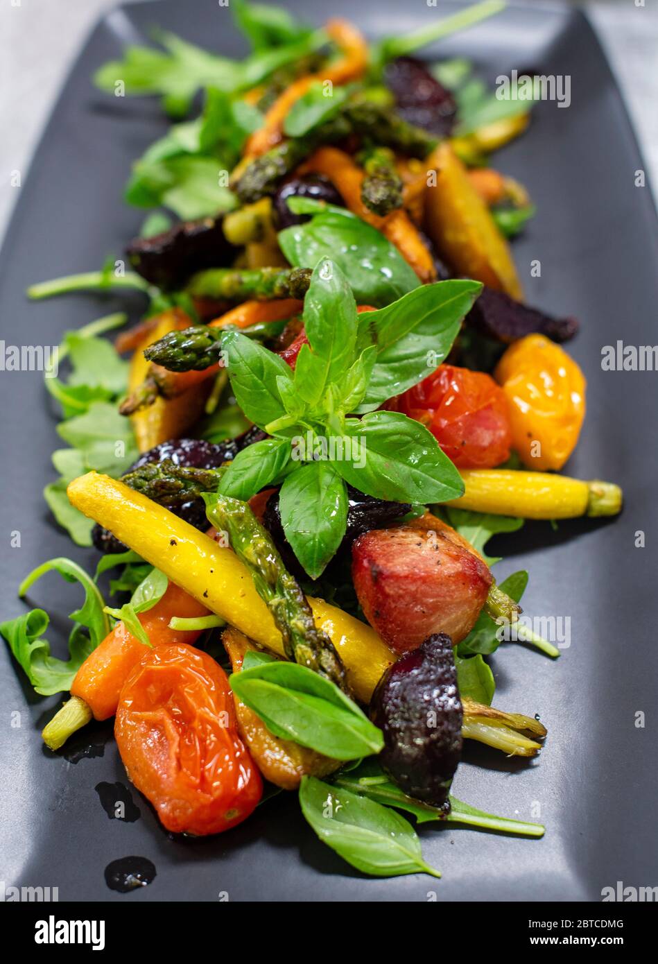 Roasted vegetables on a bed of rocket with basil drizzled with olive oil and balsamic Stock Photo