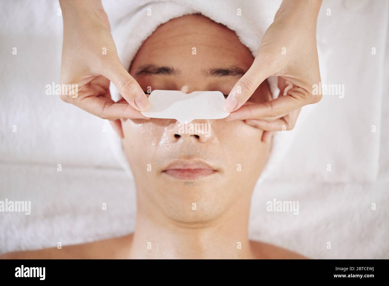 Cosmetologist applying nose strip on nose of young man to clear pores Stock Photo