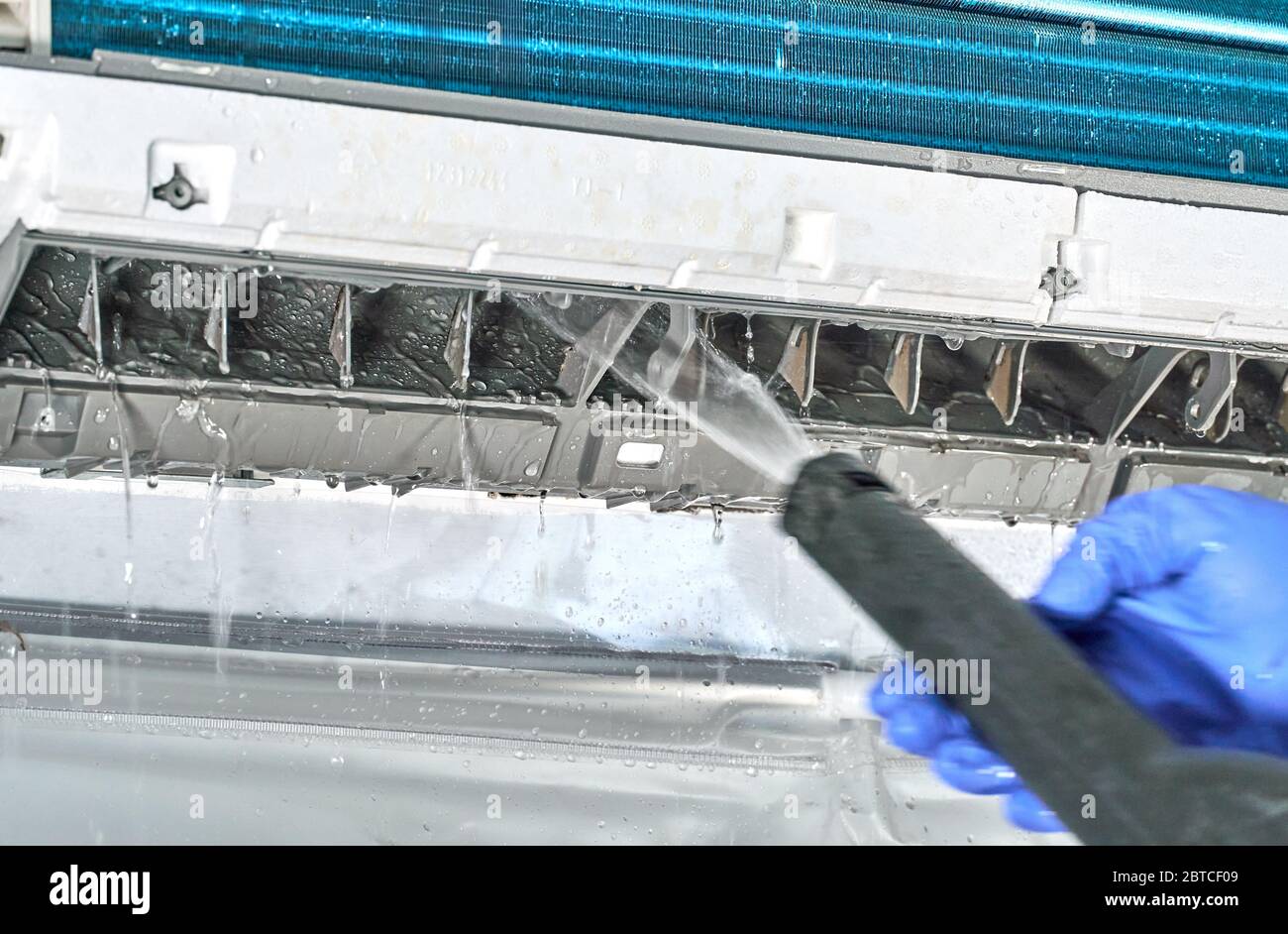 Engineer in blue gloves and mask cleaning dirty air conditioner from