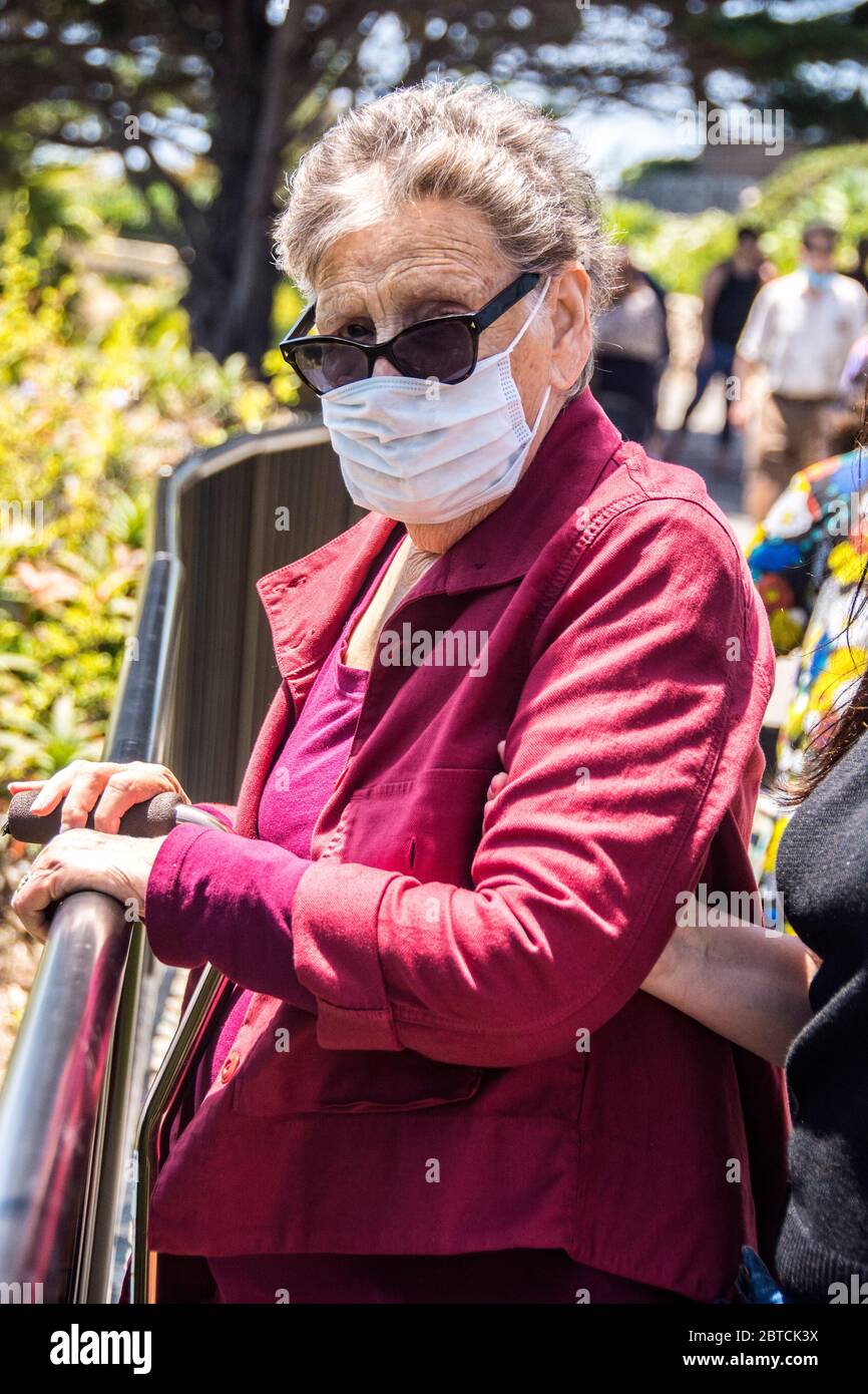 An older woman, 83, wearing a mask, standing by a fence, while on a stroll in Laguna Beach, California, USA. Stock Photo
