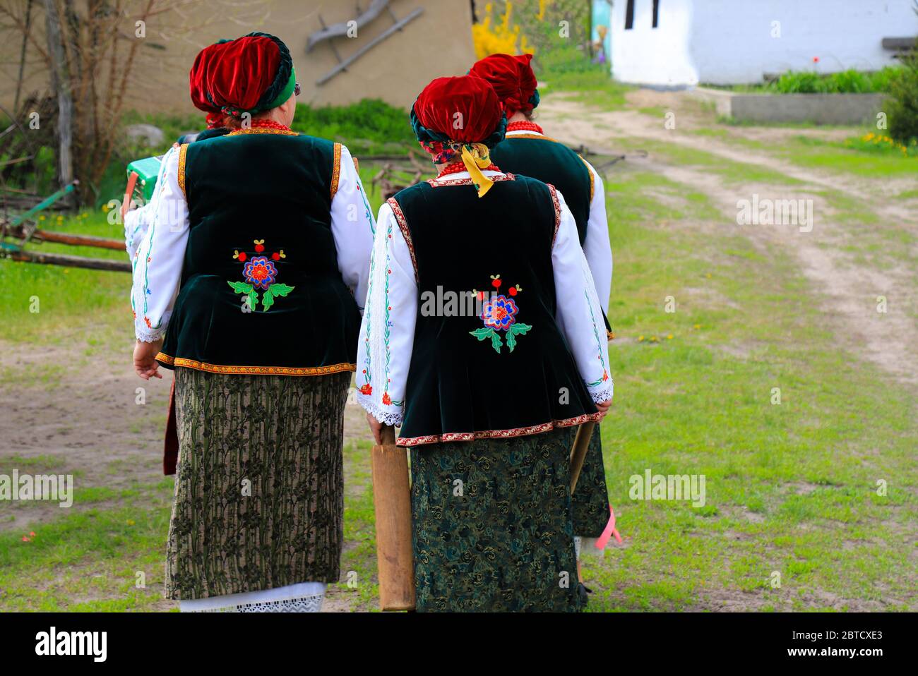 Elderly women in Ukrainian national costumes, embroidered shirts and waistcoat are walking at ethnic festival in rural landscape. Spring, summer Stock Photo