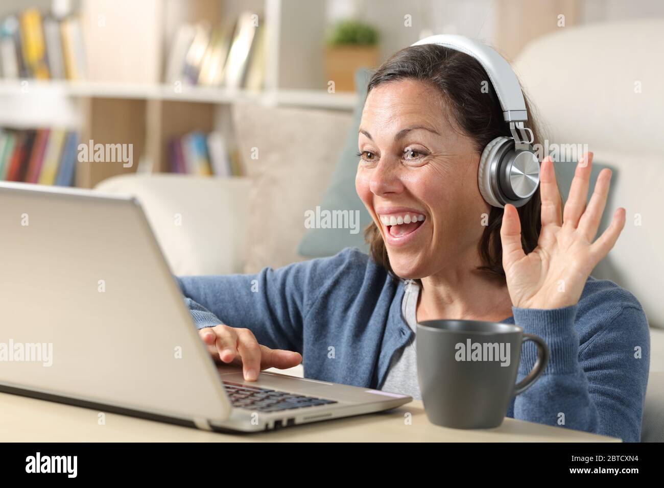 Happy adult woman videocalling with headphones on laptop webcam sitting on the floor at home Stock Photo