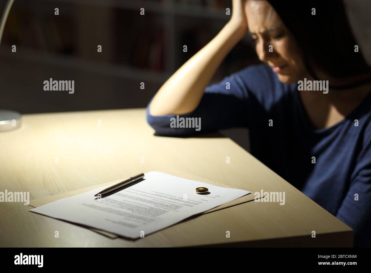 Sad wife complains after signing divorce papers and wedding ring over the table sitting at home at night Stock Photo