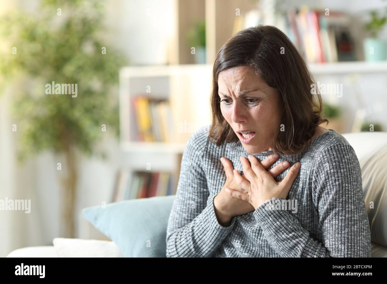 Middle age woman wheezing touching chest sitting on a couch at home Stock Photo