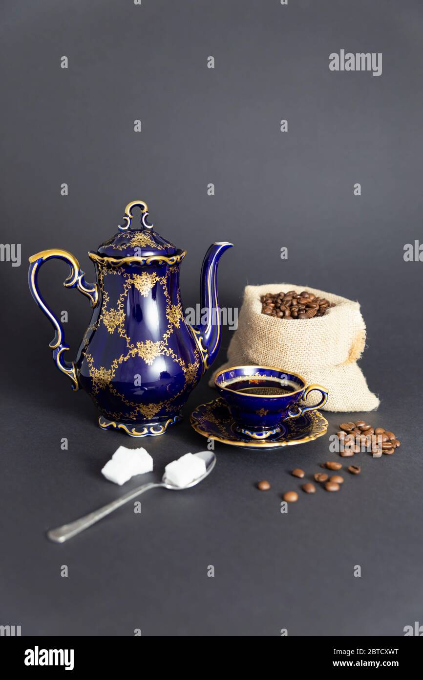 Still life with a cobalt blue vintage porcelain coffee set with golden floral pattern, a spoon with sugar cubes and a gunnysack with coffee beans Stock Photo