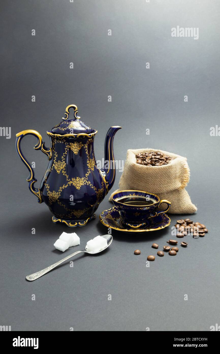 Still life with a cobalt blue vintage porcelain coffee set with golden floral pattern, a spoon with sugar cubes and a gunnysack with coffee beans Stock Photo