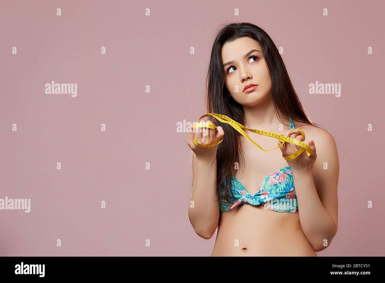 young beautiful slender Asian girl in a swimsuit . with a measuring tape in  his hands. on a pink isolated background Stock Photo - Alamy