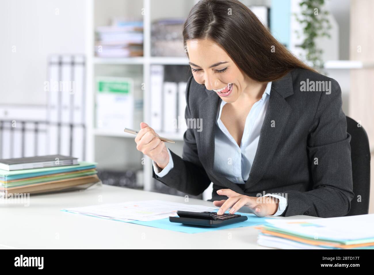 Excited bookkeeper woman checking calculator results sitting on a desk at the office Stock Photo