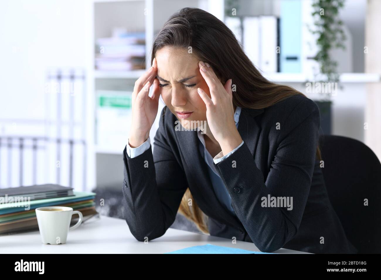 Sick executive with migraine complaining in pain rubbing temples sitting on a desk at office Stock Photo