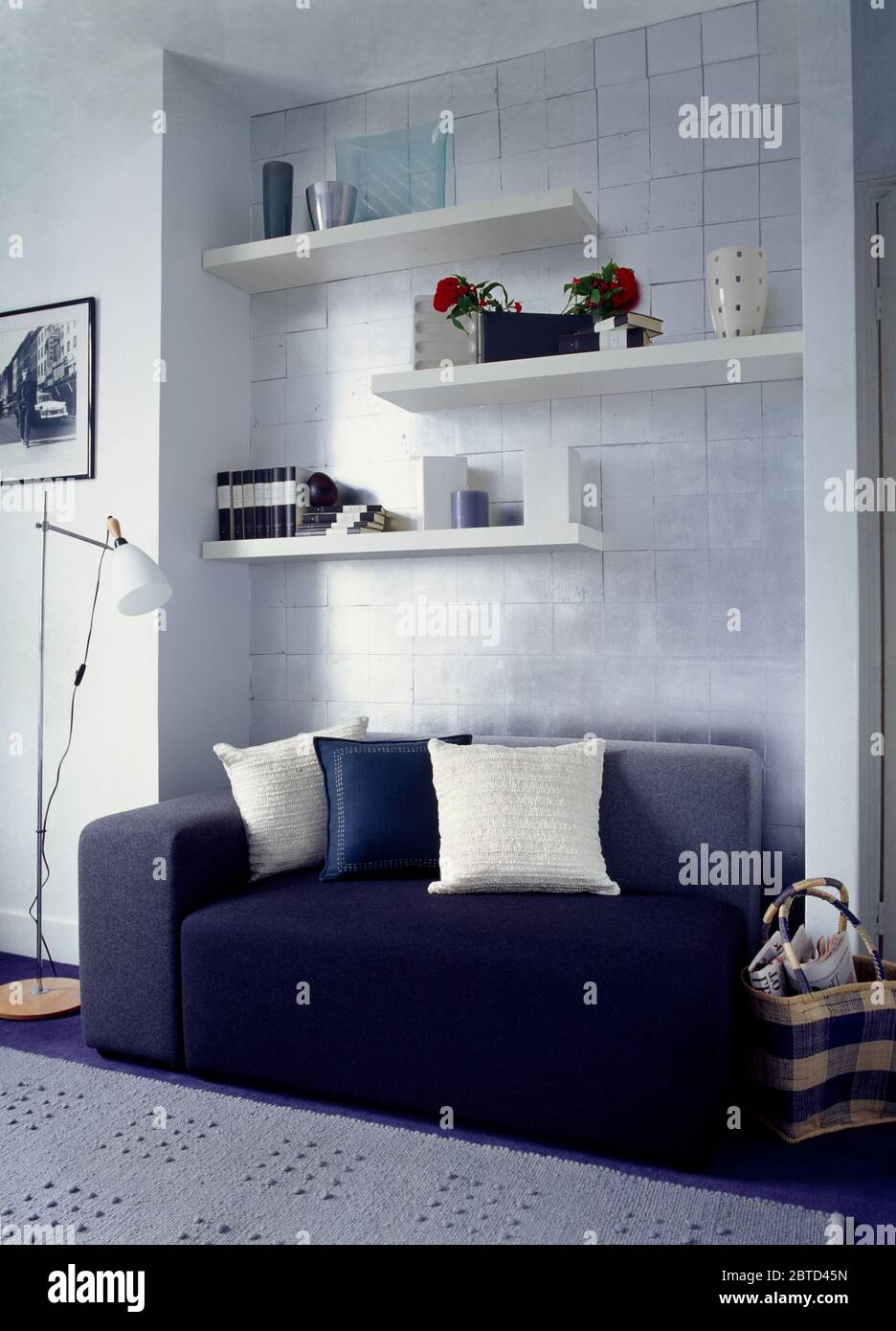 Shelving on tiled wall above blue sofa with white cushions Stock Photo
