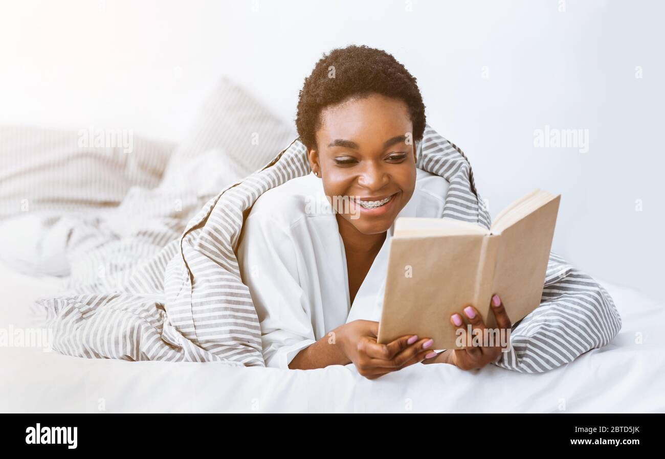 Morning book reading. African american woman wrapped in blanket Stock