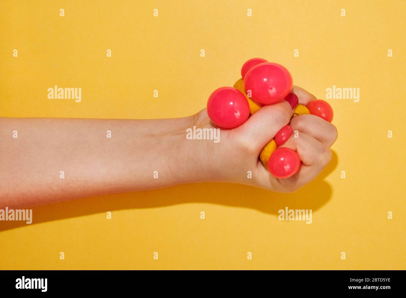 Hand squishing a colorful toy ball belonging to a child over a bright yellow background with shadow and copy space Stock Photo