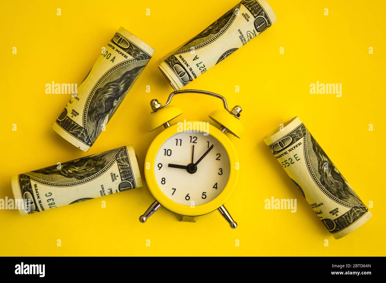 alarm clock both monetary denominations dollars, Time is money. Retro alarm clock and hundred dollar bills on a yellow background Stock Photo